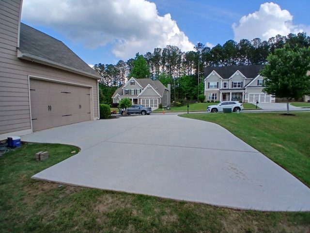681d27d0c25be_221679824 A driveway with cars parked in it and houses on the other side of the road.