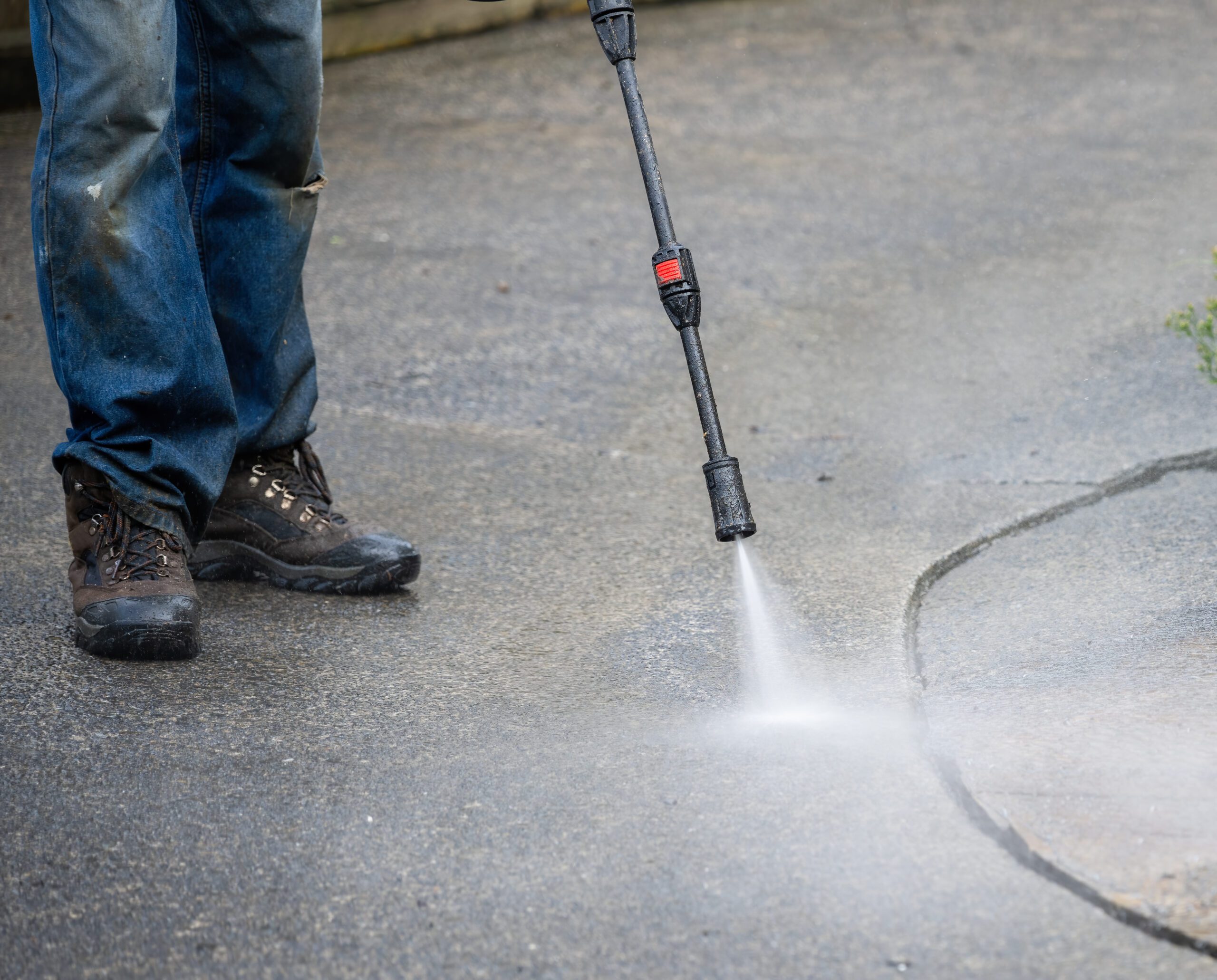 Worker cleaning pavement using an electric water blaster. A person using a power washer on the sidewalk.