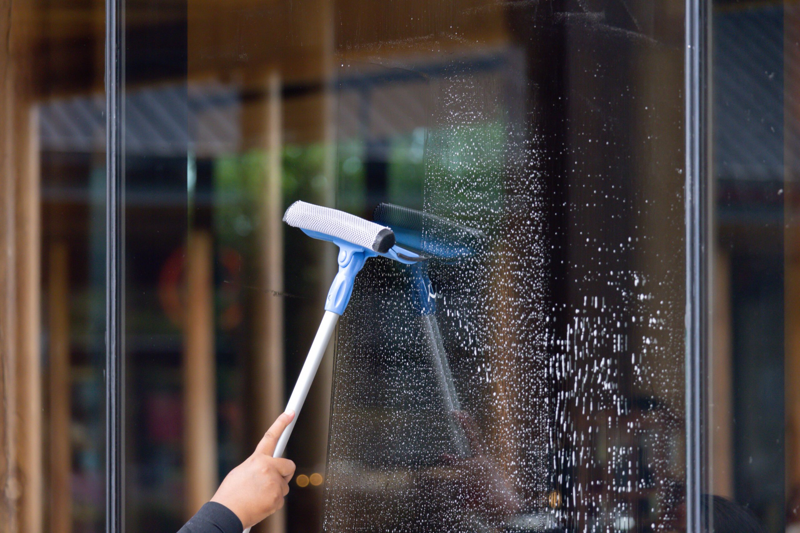 A person is cleaning a window with a squeegee A person using a window cleaner on a glass