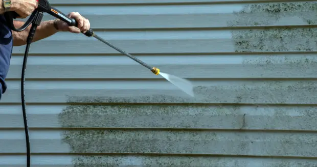 A person using a power washer on the side of a house.
