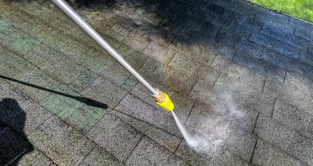 A person using a hose to clean the roof of a house.